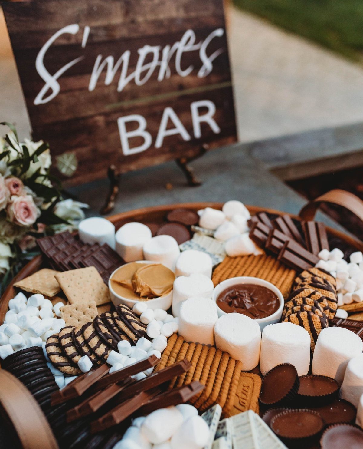 S'mores bar tray with marshmallows, chocolate, and graham crackers next to a wooden sign.