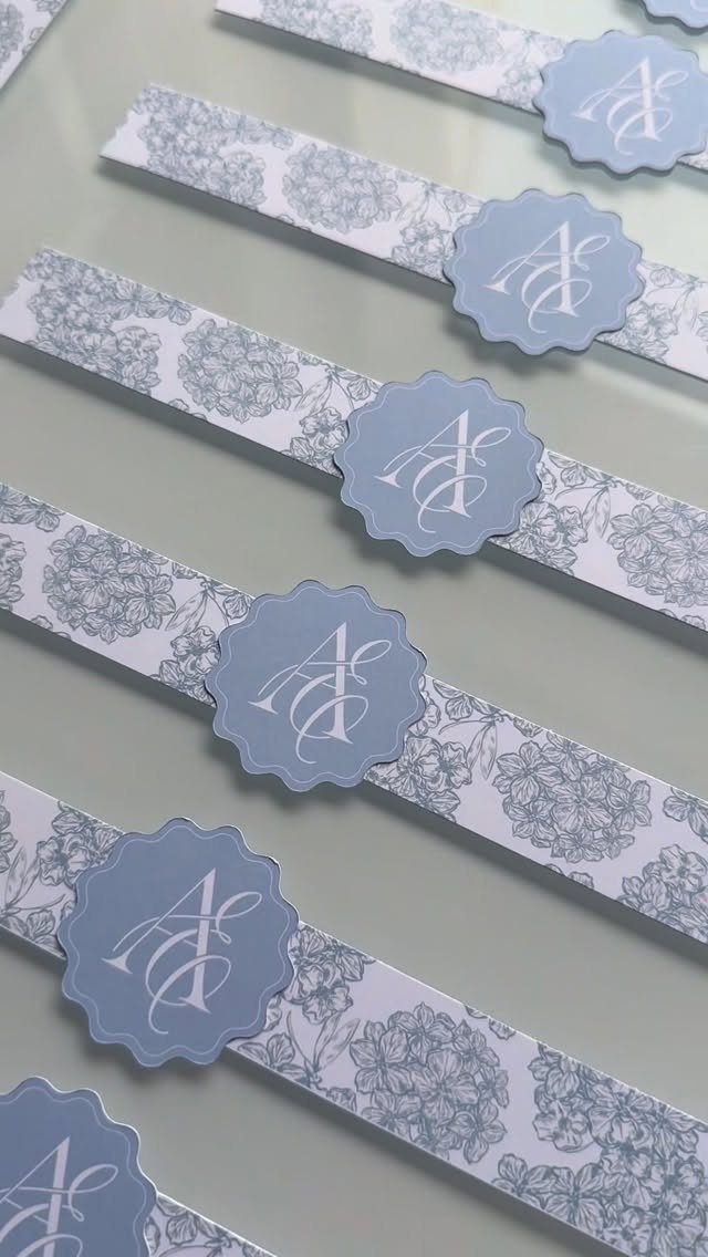 Floral patterned belly bands with scalloped monogram seals for wedding invitations.