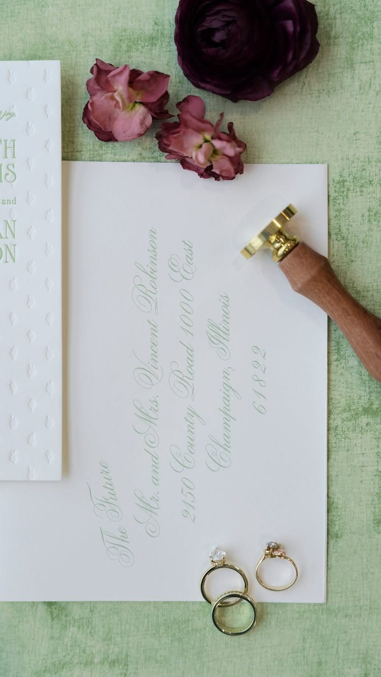 White envelope with calligraphy addressing surrounded by flowers, rings, and a wax seal.