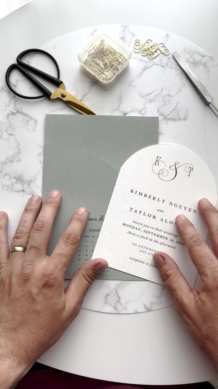 Sage green wedding envelope and white invitation card on a marble tabletop.
