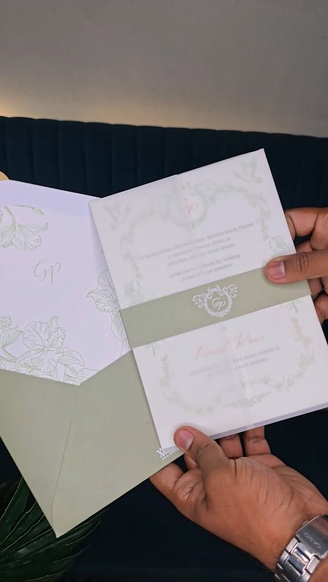 Wedding invitation suite with sage green envelope and belly band held by hands.