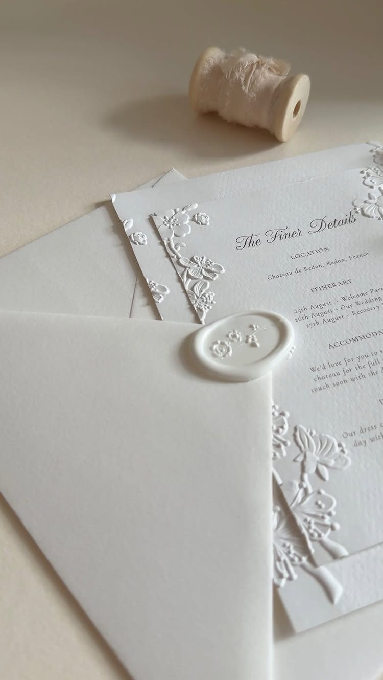 White wedding invitation cards with embossed floral lace and a wax sealed envelope.