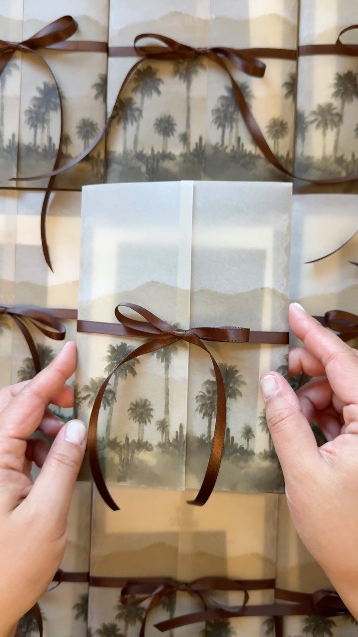 Wedding invitation with a brown satin ribbon tied in a bow and palm trees.