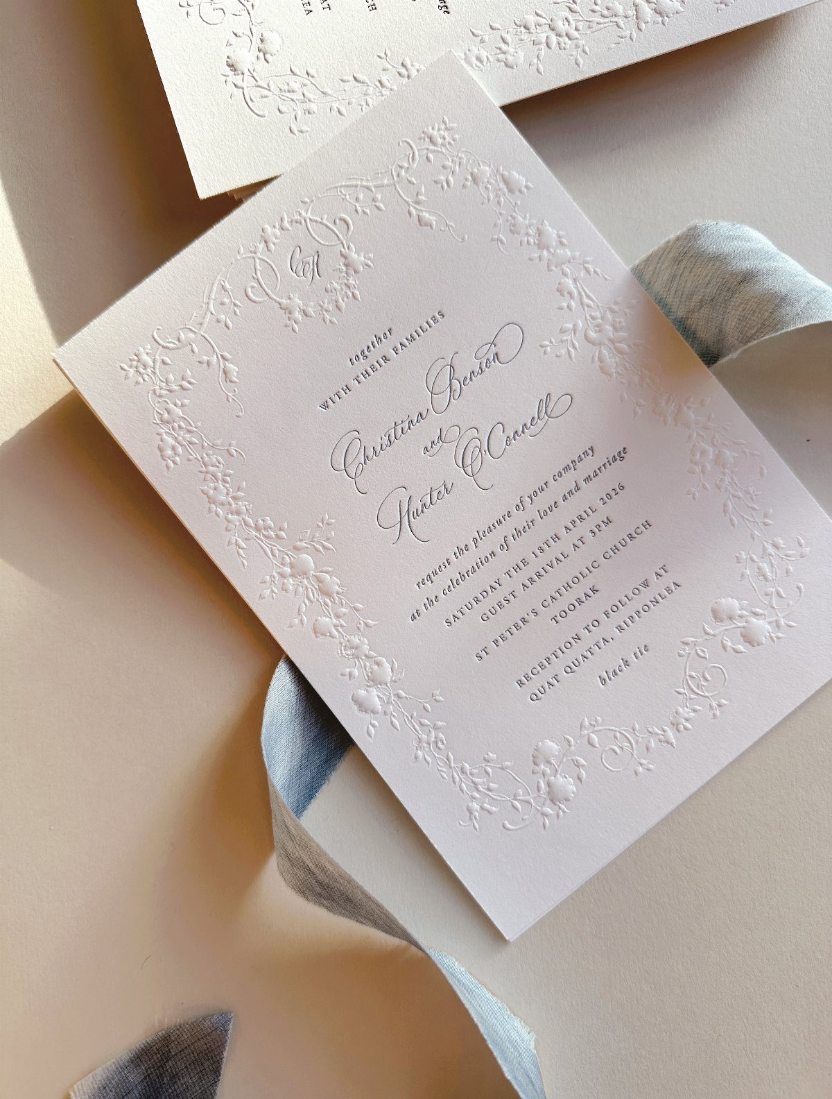 White embossed wedding invitation card accented with a flowing light blue silk ribbon.