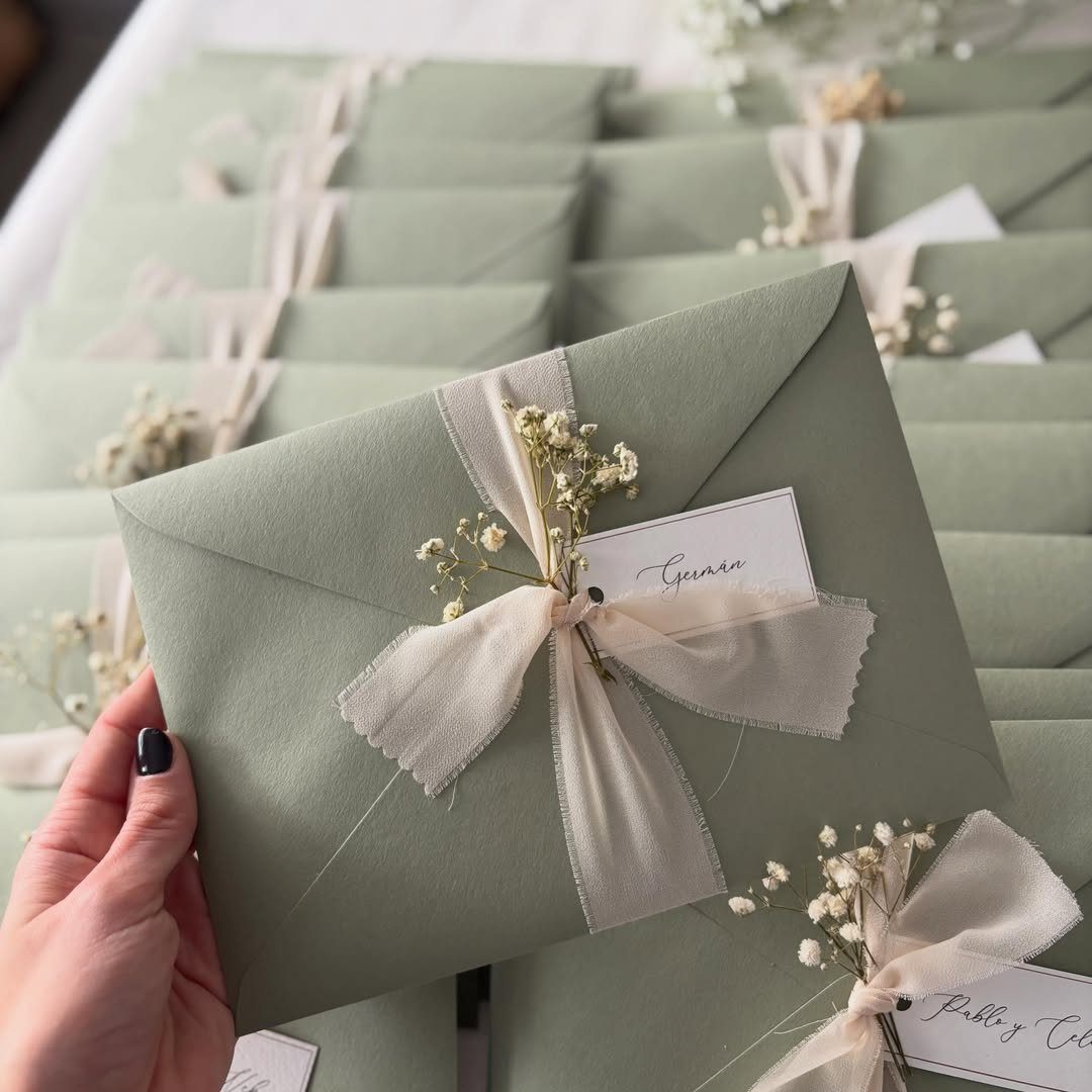 Sage green envelope tied with a cream frayed ribbon bow and dried flowers.