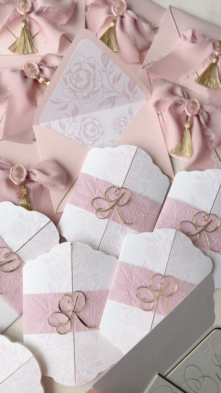 White and pink wedding invitations wrapped in pink ribbons with gold wire bows.