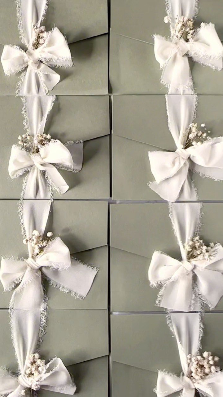 Sage green envelopes tied with white ribbons and small white dried flowers.