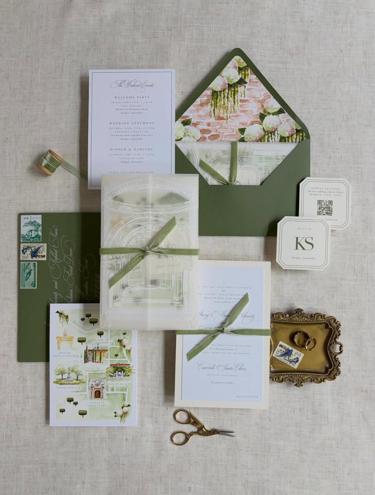 Wedding invitation suite with olive green ribbons, envelopes, and gold scissors on linen.