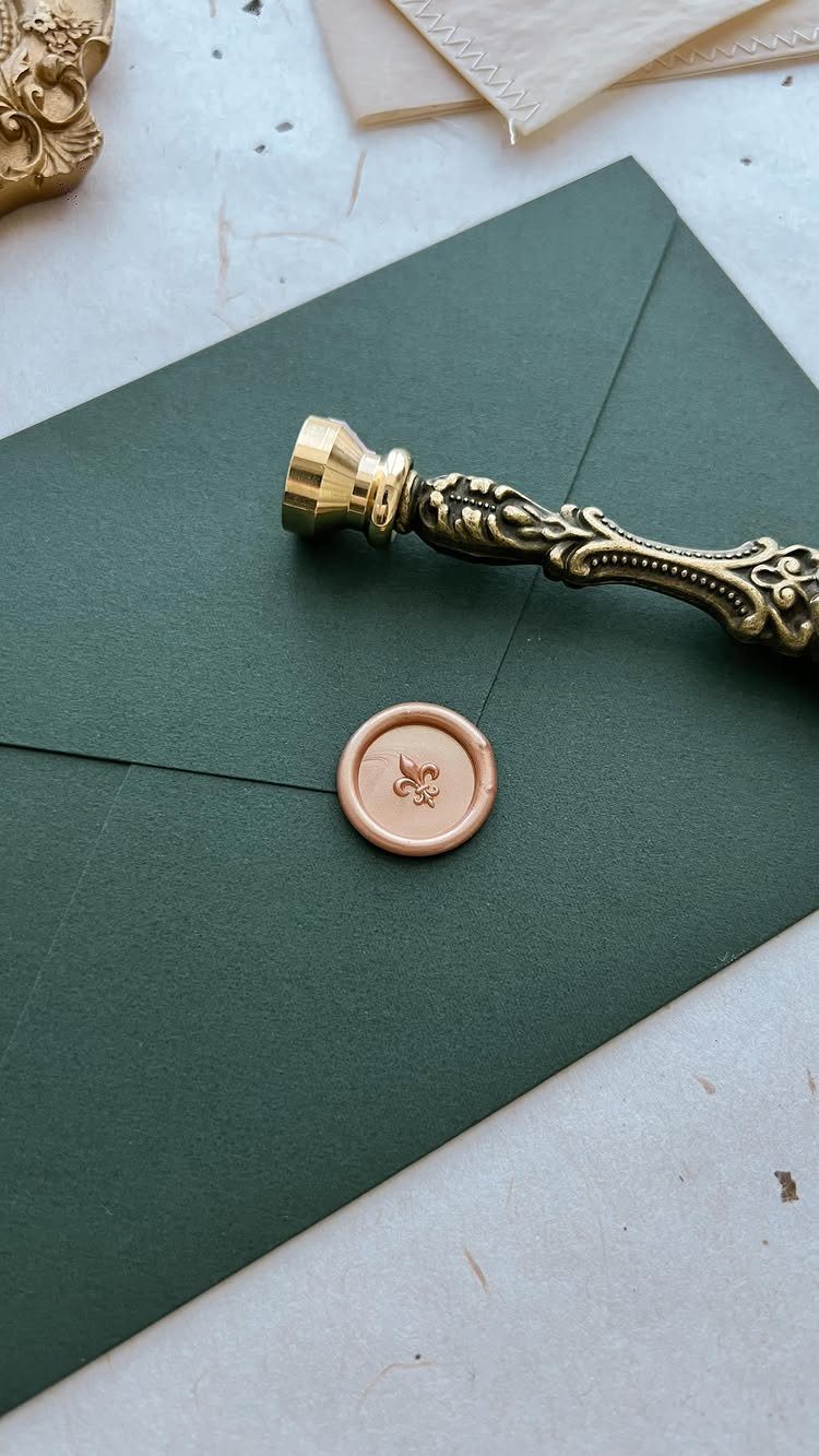 Peach wax seal on a dark green envelope flap with a gold stamp.