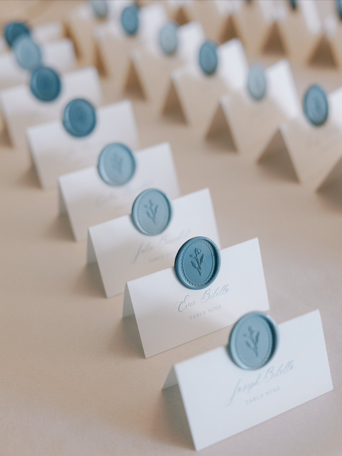 White folded place cards with blue botanical wax seals arranged in neat rows.