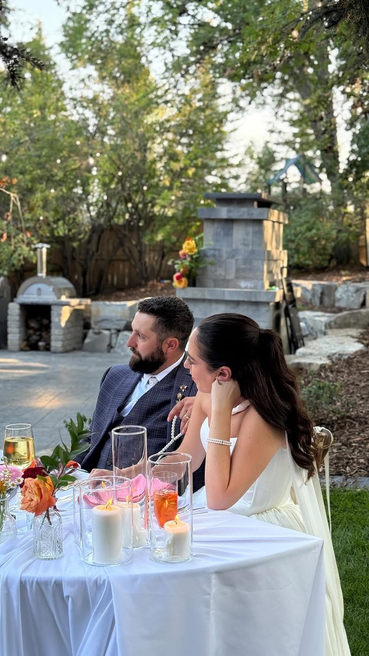 Bride and groom sitting at a decorated table in a residential backyard setting.