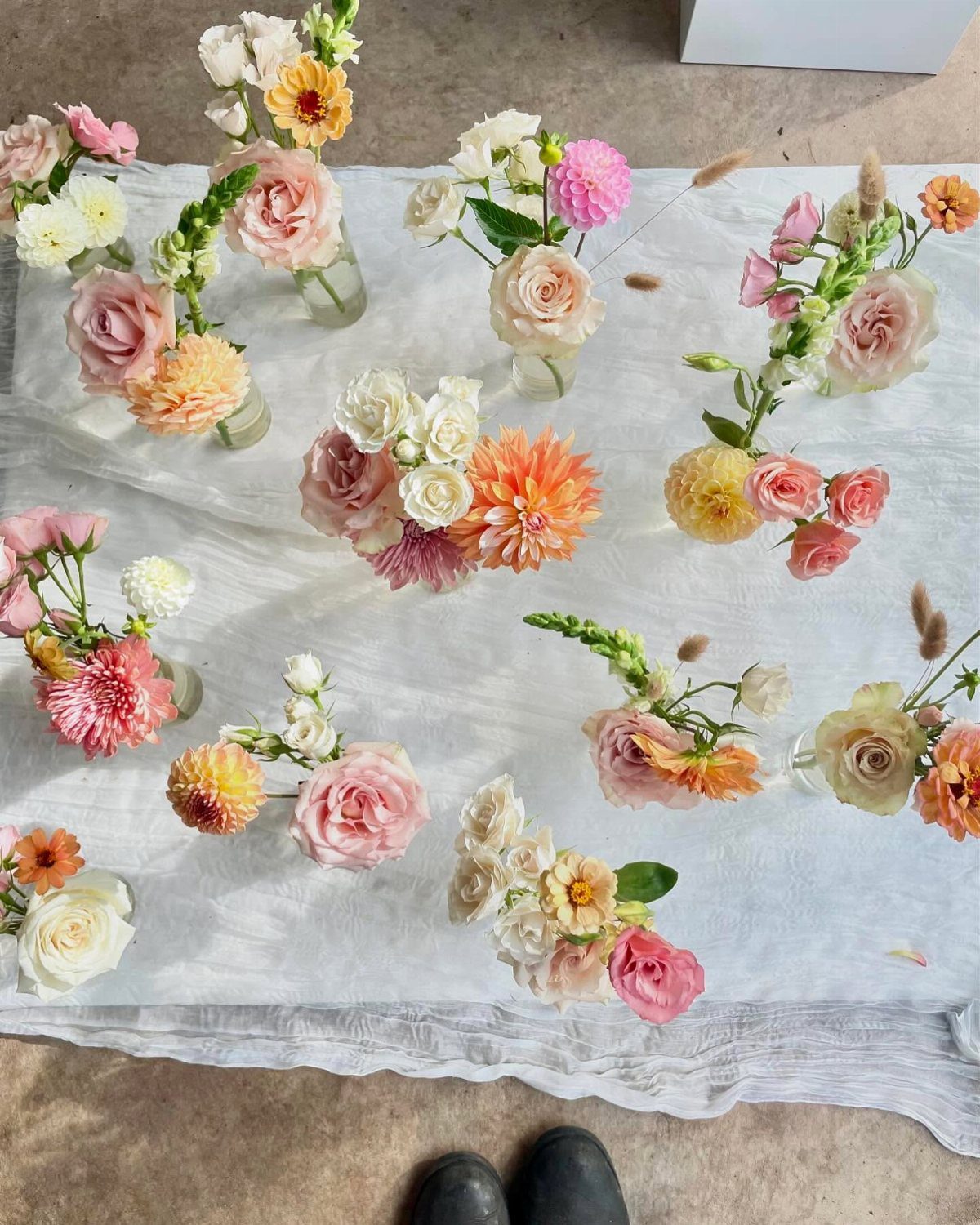Small glass vases with pastel pink and orange flowers on white fabric.