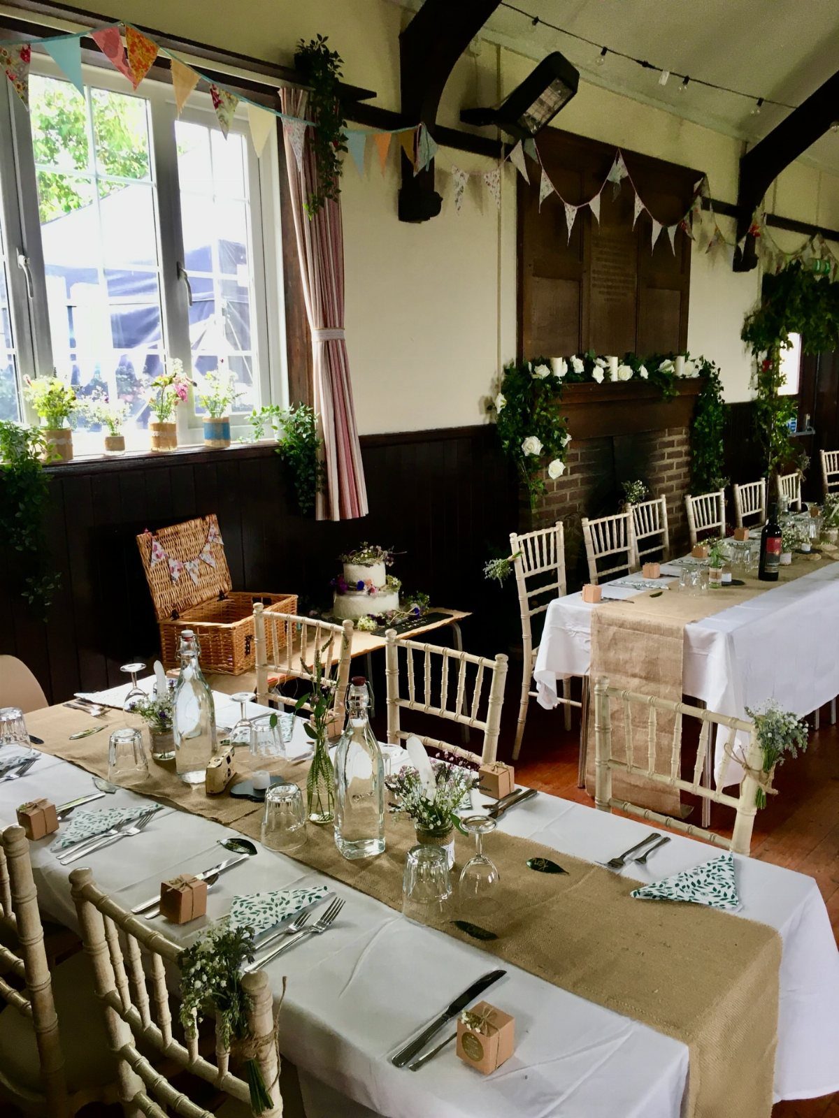 Rustic wedding reception tables with burlap runners, simple jar flowers, and colorful bunting.