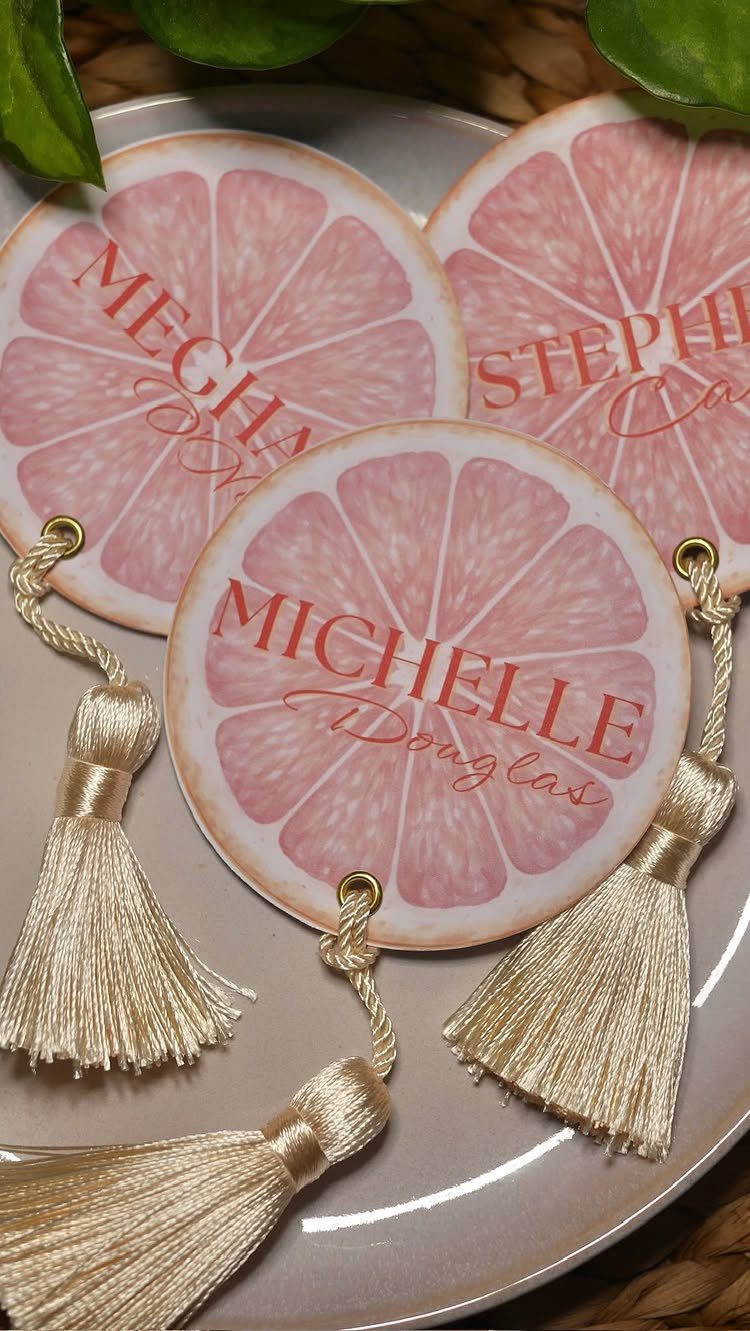 Circular pink grapefruit name tags with gold tassels resting on a white plate.
