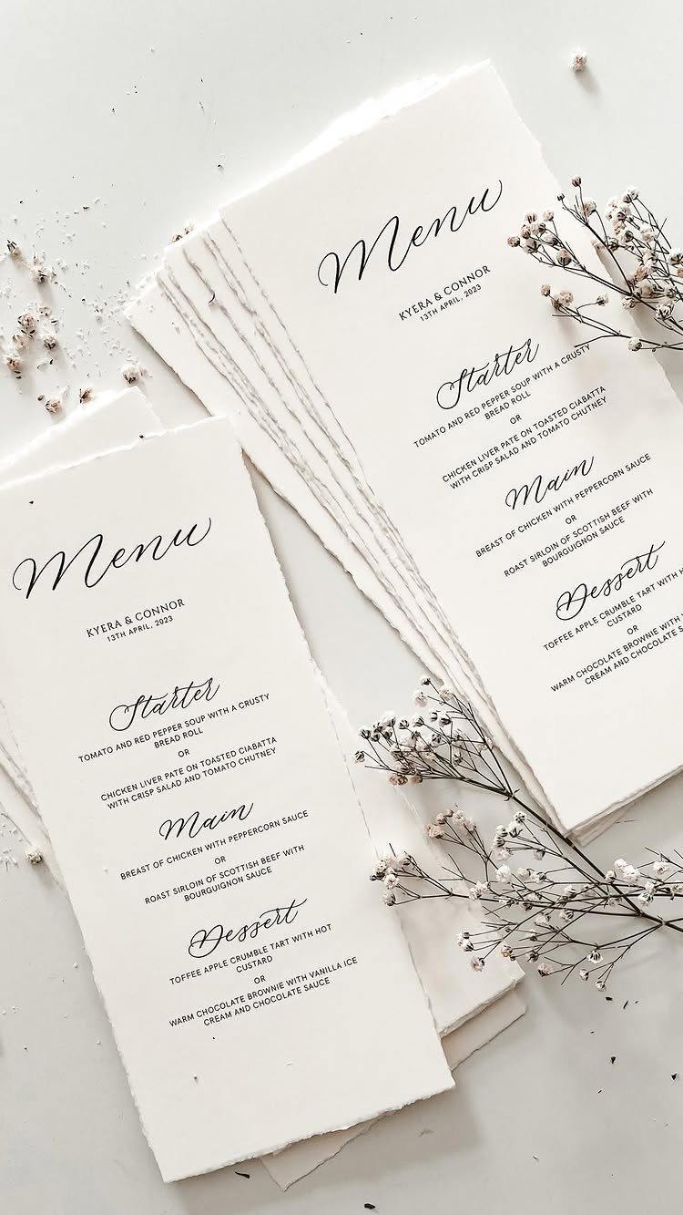 White deckle-edged wedding menus with black text and dried baby's breath flowers.