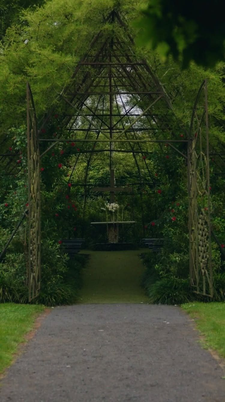 Green vine-covered metal gazebo with a small altar in a lush garden setting