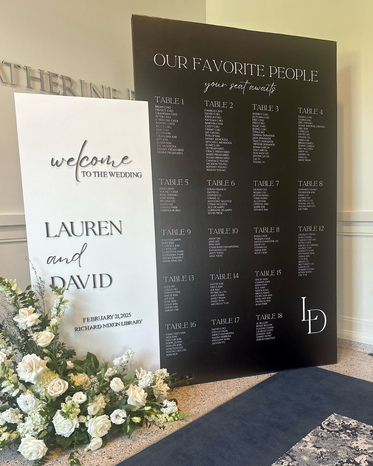 Black wedding seating chart board and white welcome sign with white floral arrangements.