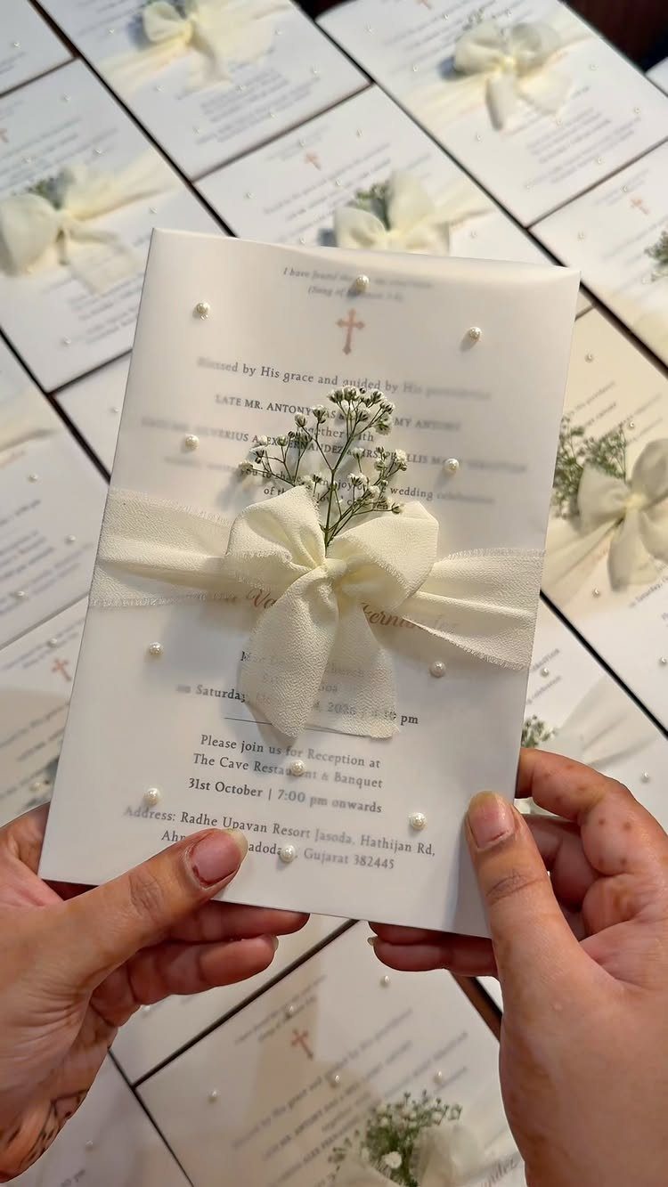 White wedding invitation card with a cream ribbon bow and baby's breath flowers.