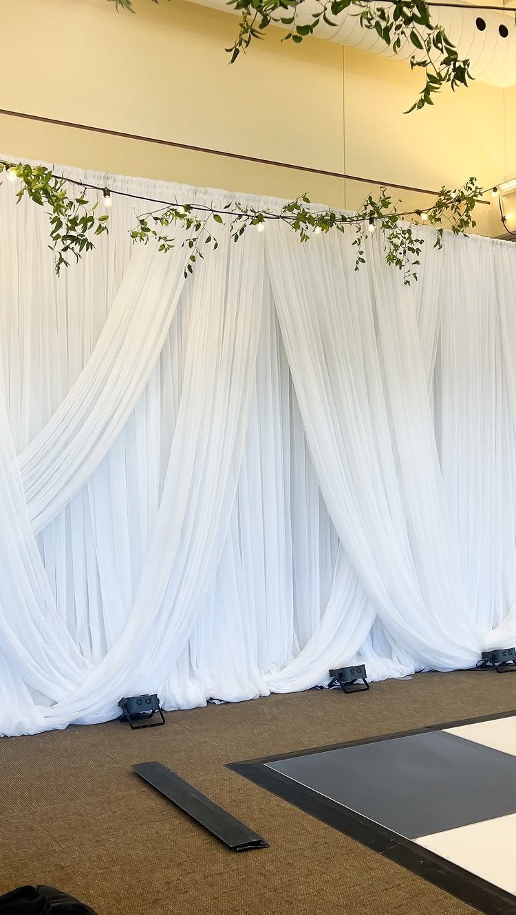 White draped fabric backdrop with fairy lights and green vines for wedding decor.