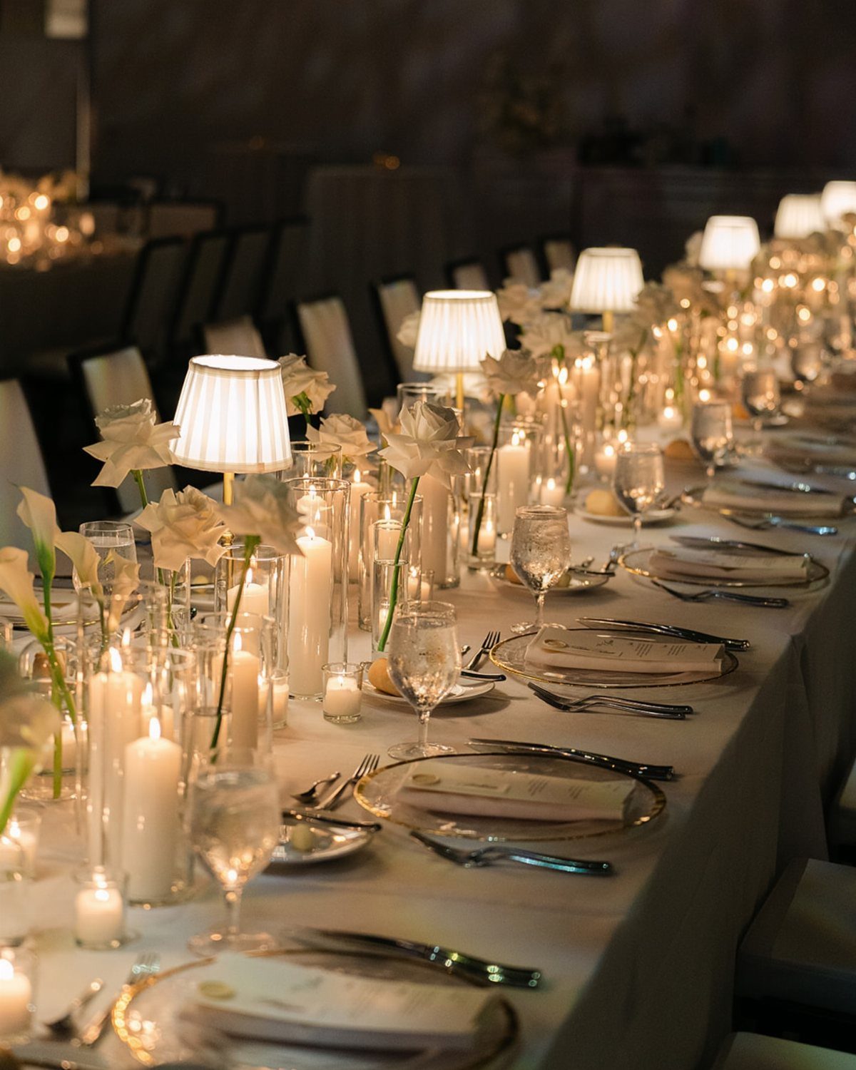 Long wedding table set with white linens, numerous glowing candles, and white flowers.