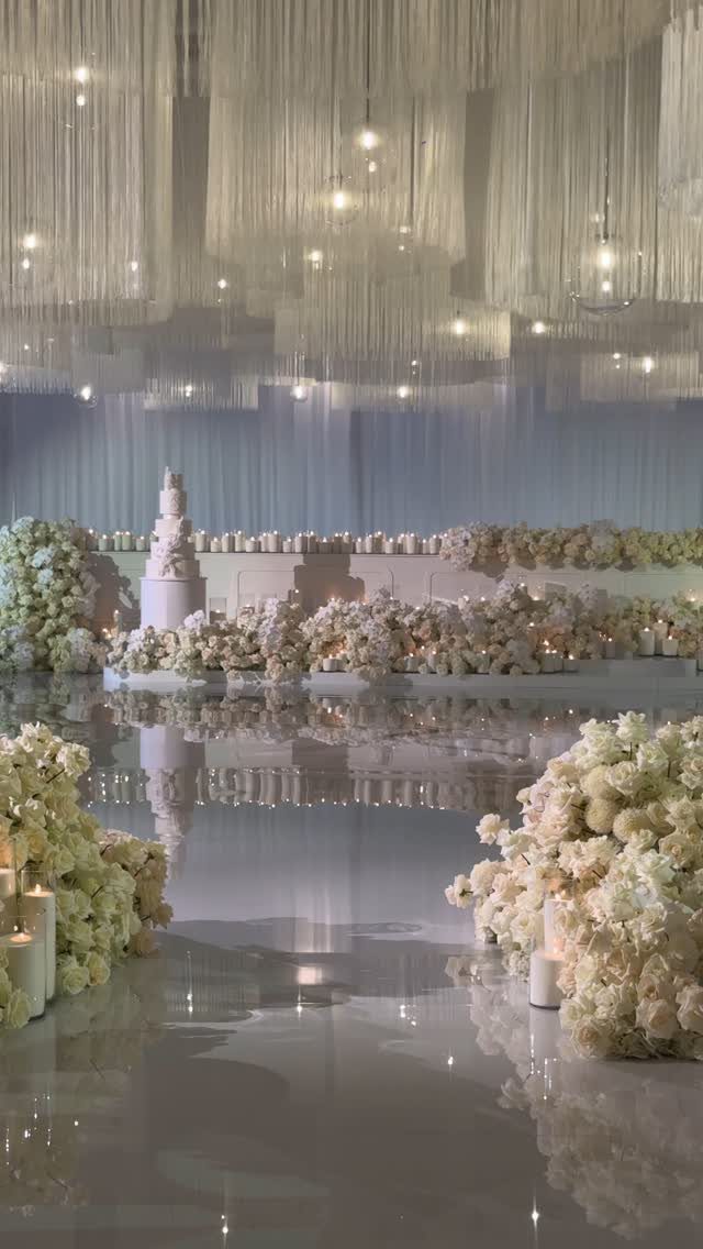 Luxurious wedding reception with white flowers, a tiered cake, and reflective floors.