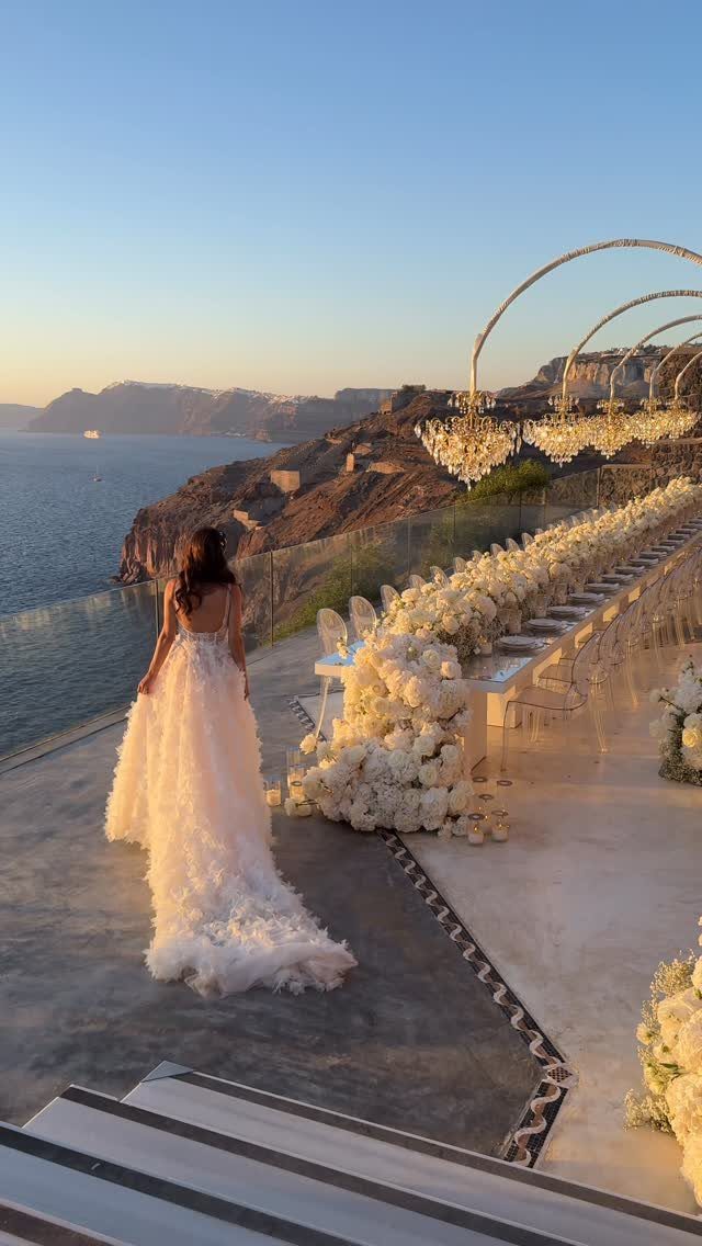 Bride in white gown overlooking a luxury cliffside wedding table with white flowers