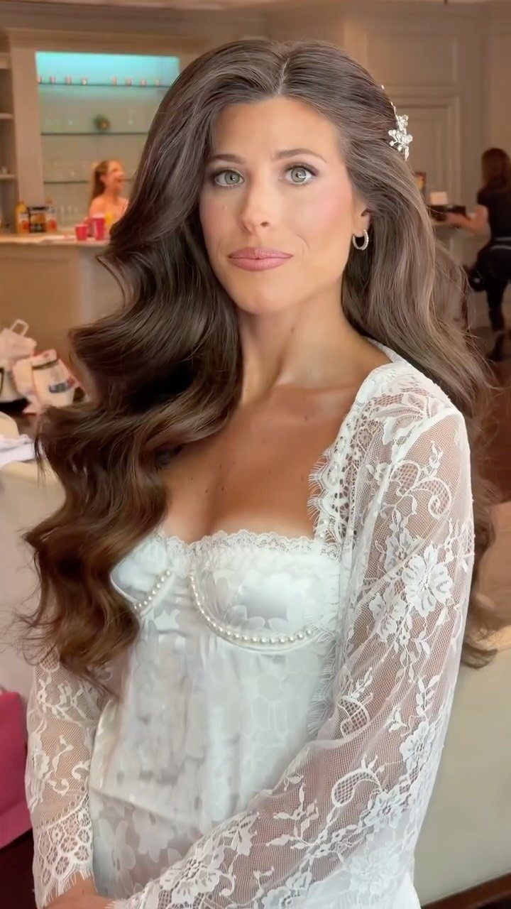 Woman with wavy brown hair and bridal makeup wearing a white lace robe.