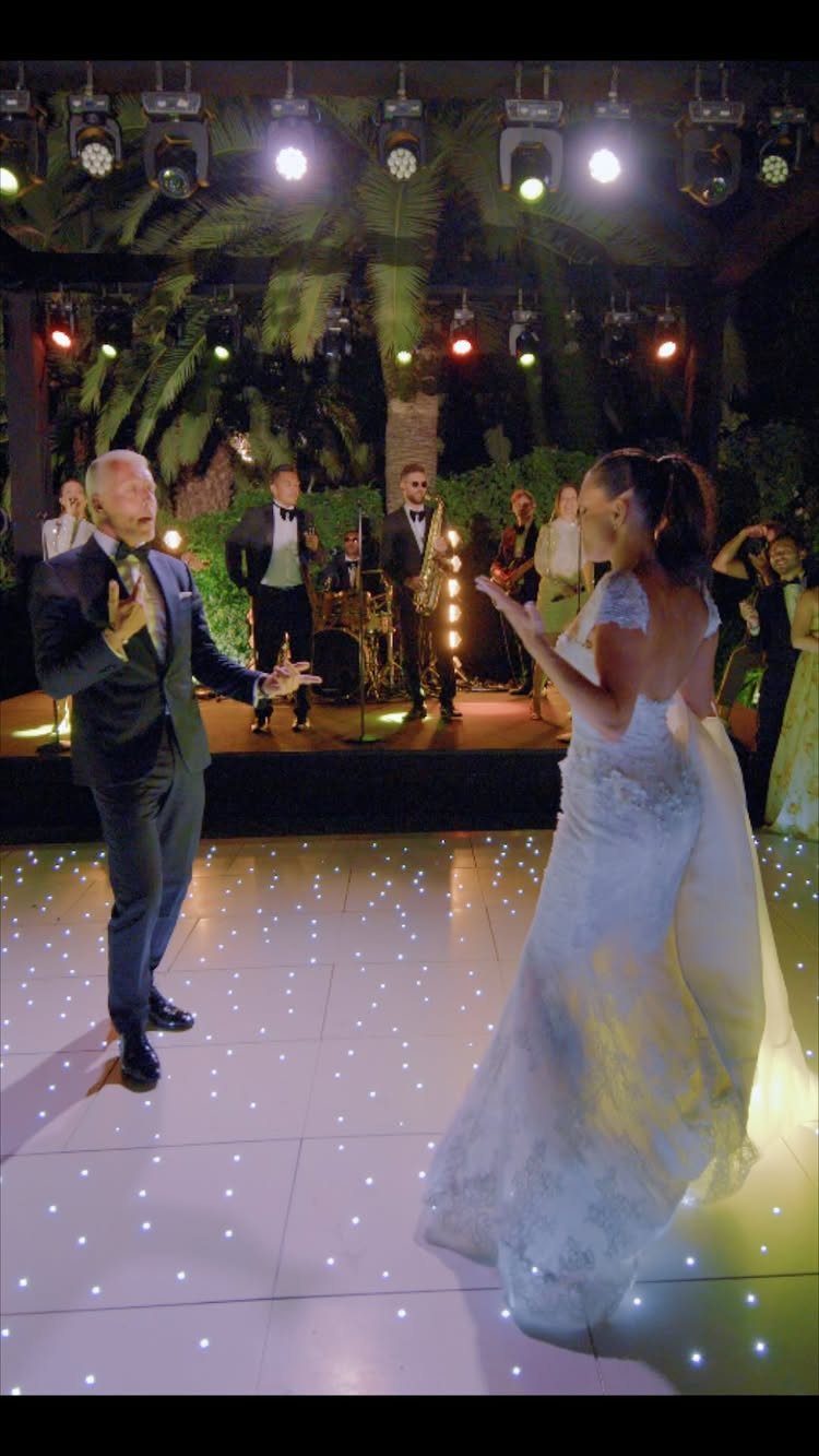 Bride and groom dancing on a lit floor with a live band performing behind them.