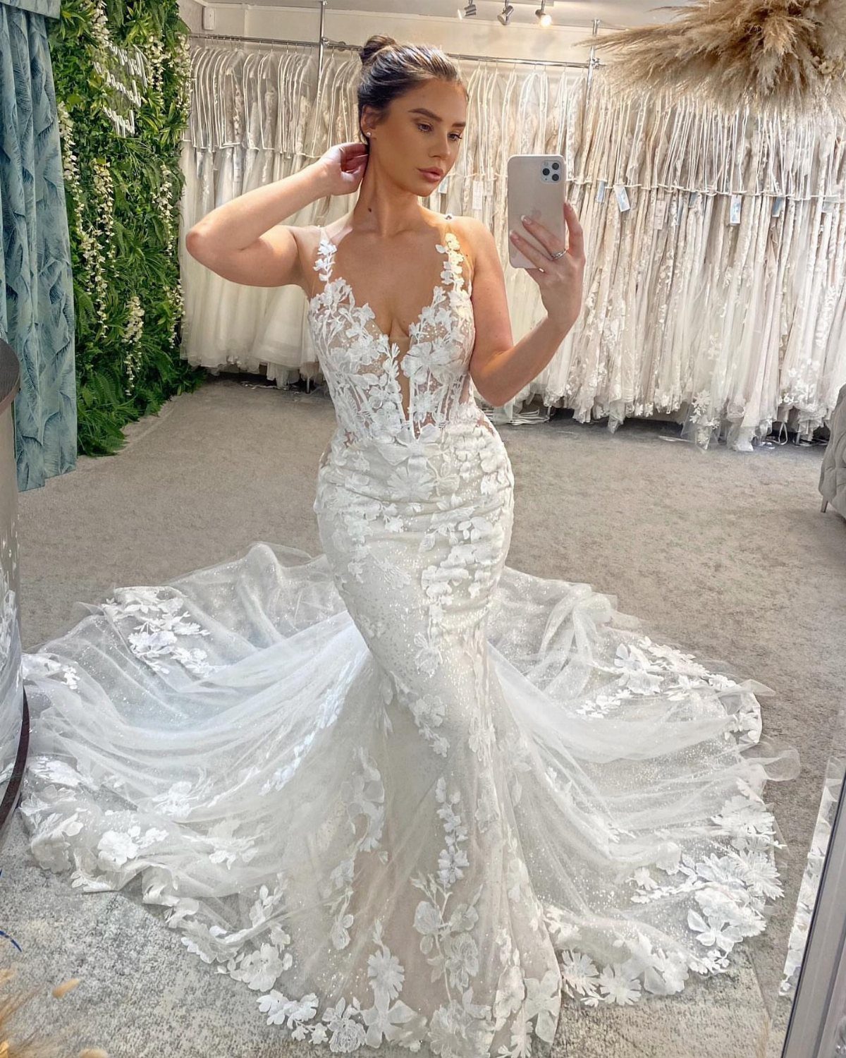 Woman in a white lace mermaid wedding dress taking a mirror selfie in boutique
