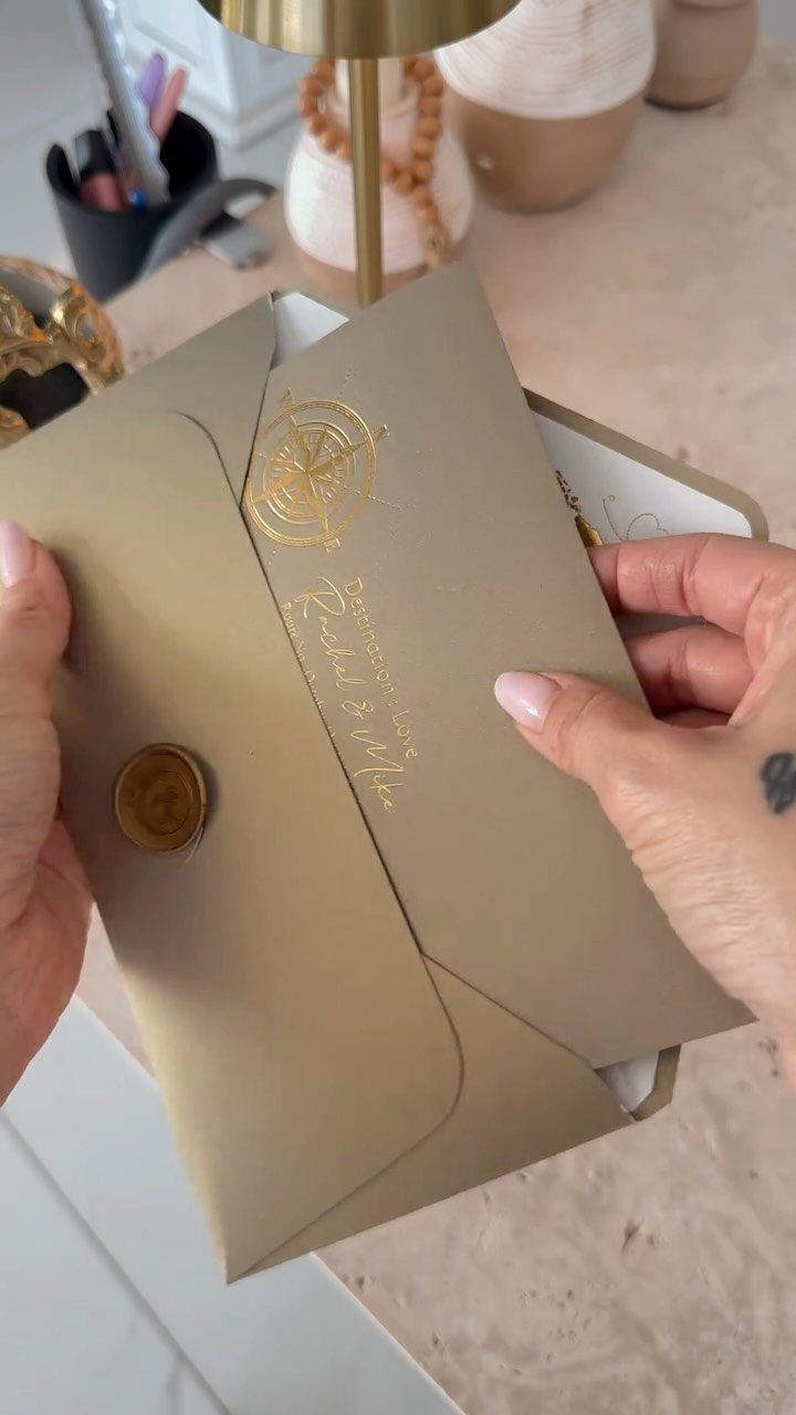 Gold envelope with wax seal and calligraphy being opened by two hands.