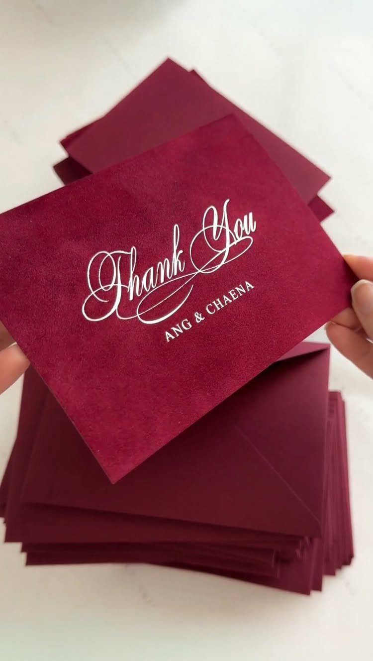 Burgundy thank you cards and matching envelopes held by a person's hands.