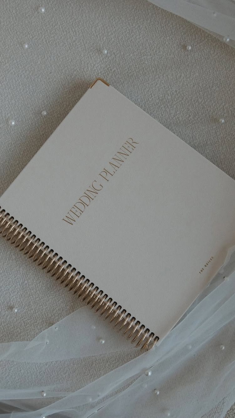 White spiral wedding planner notebook resting on a pearl-studded white bridal veil.