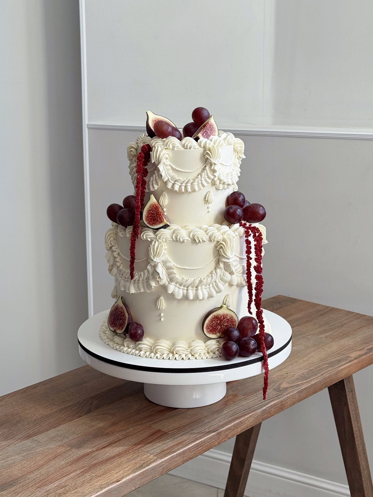 Three-tier white wedding cake decorated with fresh figs, purple grapes, and red amaranth.