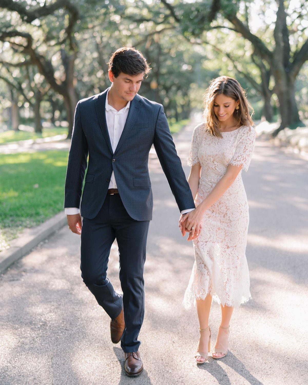 Couple holding hands and walking on a tree-lined path for engagement photos.