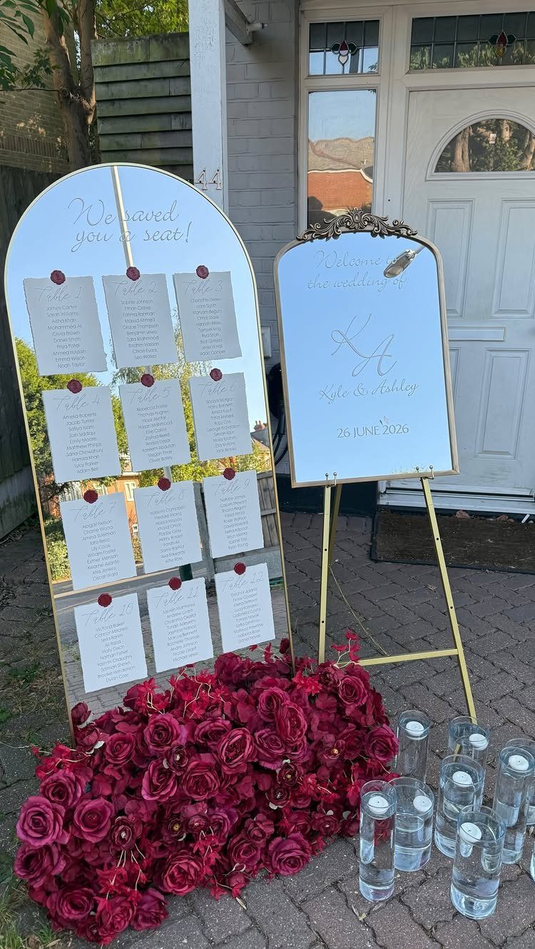 Gold-framed mirror seating chart with white lists and red roses at the base.