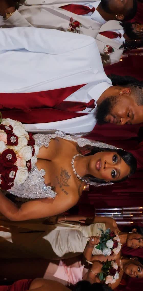 Bride in lace gown and groom in red vest posing together at wedding.