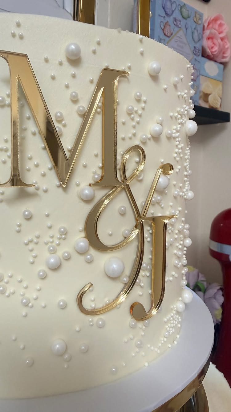White wedding cake with gold initials M and J and white pearl decorations.