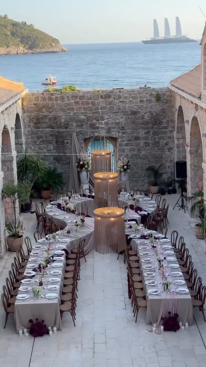 Outdoor wedding reception setup in a stone courtyard overlooking the blue ocean.