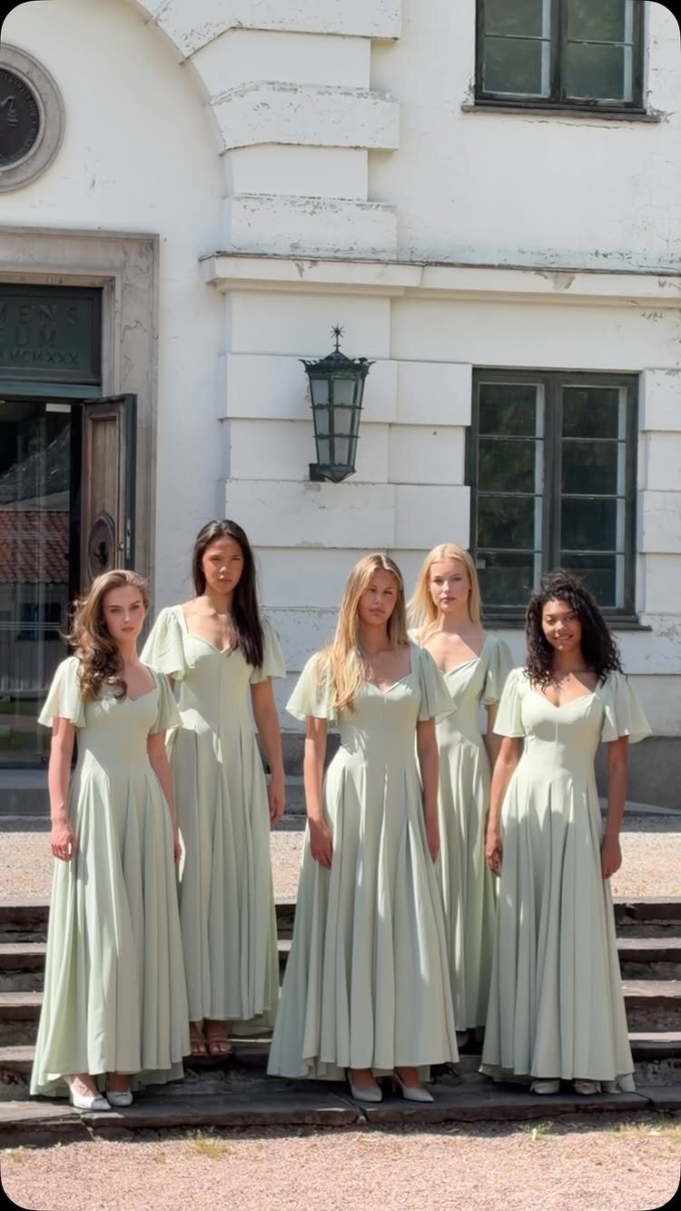 Five bridesmaids wearing matching light green gowns posing in front of a white building.