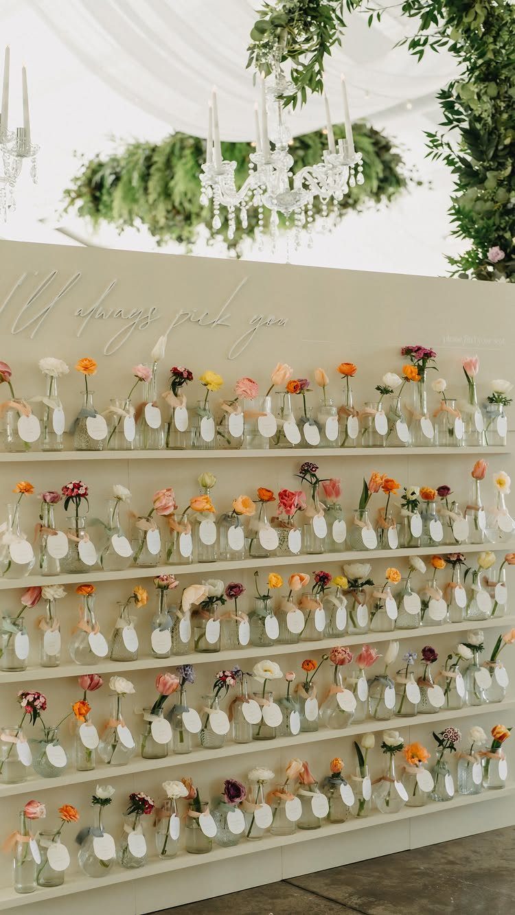 Wedding seating chart with small glass bottles holding colorful flowers and name tags.
