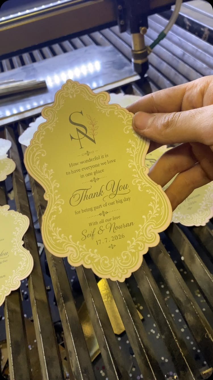 Hand holding a decorative yellow wedding thank you card over a laser cutter.