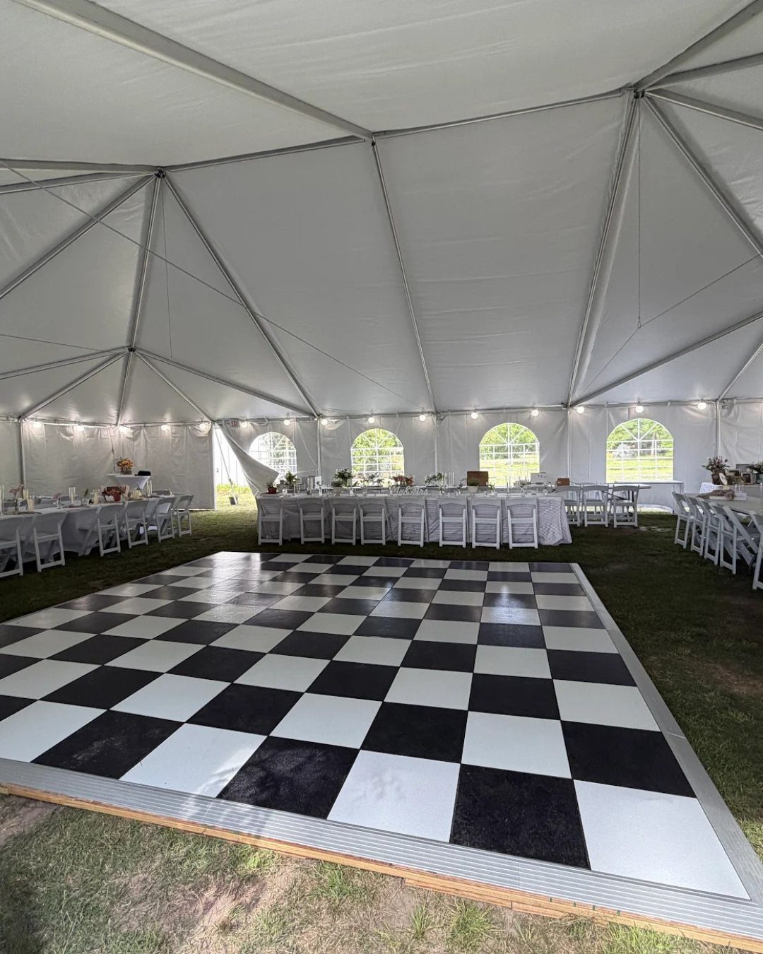 Checkered dance floor inside a white event tent with white tables and chairs.
