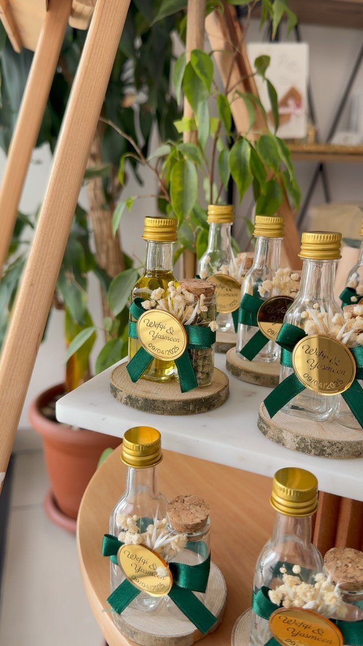 Small glass favor bottles with green ribbons and gold tags on wooden slices.