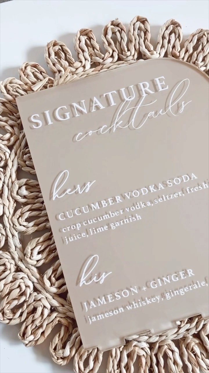Acrylic signature cocktail sign listing drinks for the bride and groom on straw mat