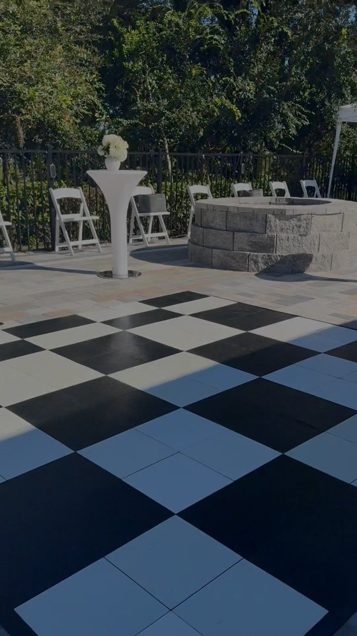 Black and white checkered portable dance floor on an outdoor stone patio with chairs.