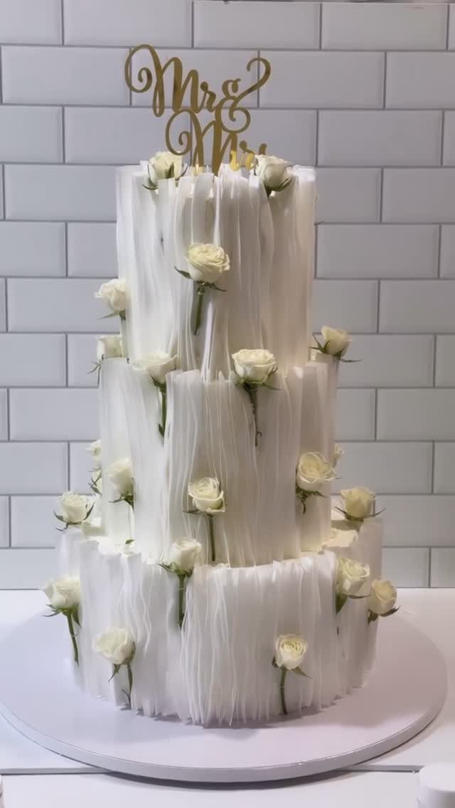 Three-tiered white wedding cake with white roses and gold Mr and Mrs topper.