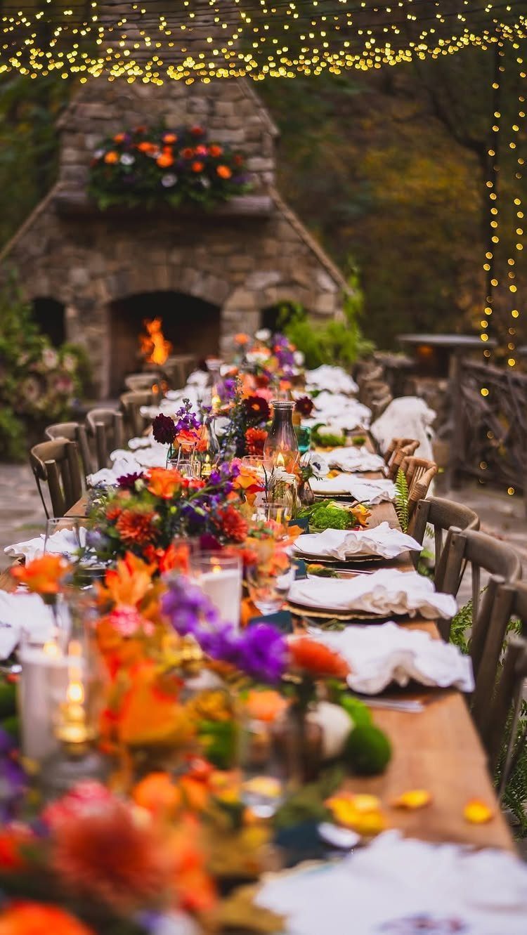 Long wooden table with colorful flowers and candles under twinkling outdoor fairy lights.