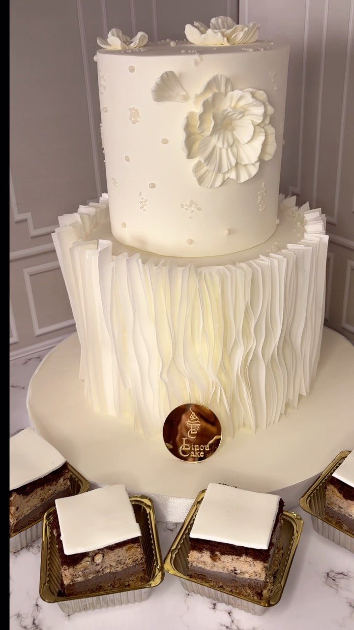 Two-tier white wedding cake with floral accents and chocolate dessert bars in gold cups.