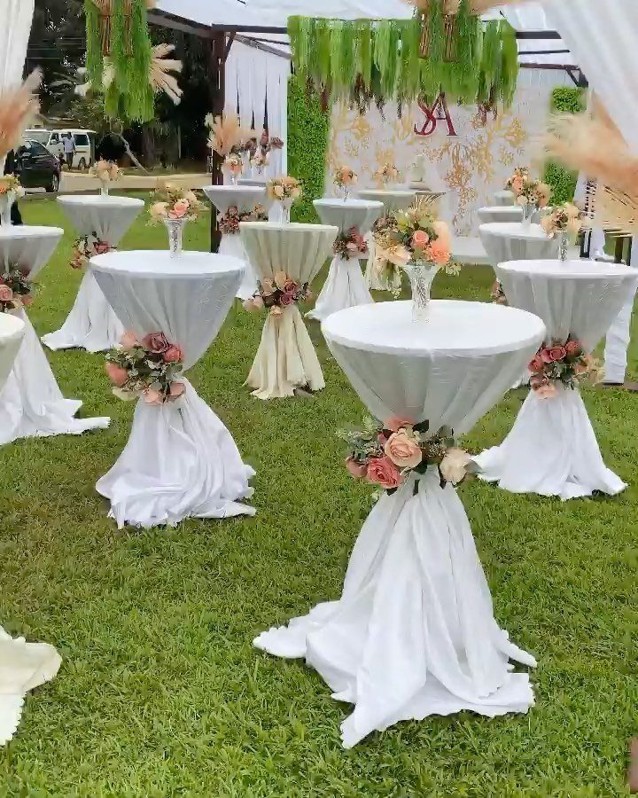 White cocktail tables with floral accents arranged on a lawn for a wedding reception.