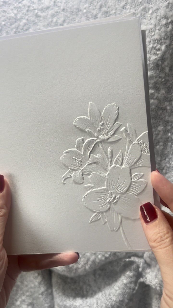 White embossed floral card held by hands with red nail polish